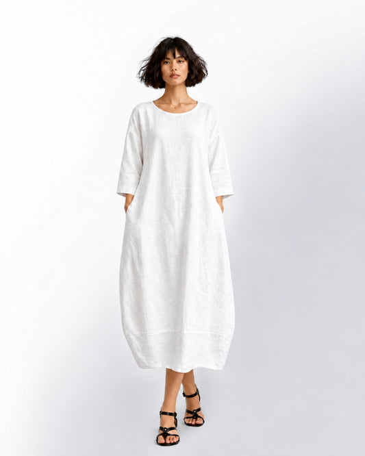 Model wearing the Jen Kahn Tokyo linen dress in white, showing three-quarter sleeves, side pockets and a tapered cocoon shape with a lower panel seam.