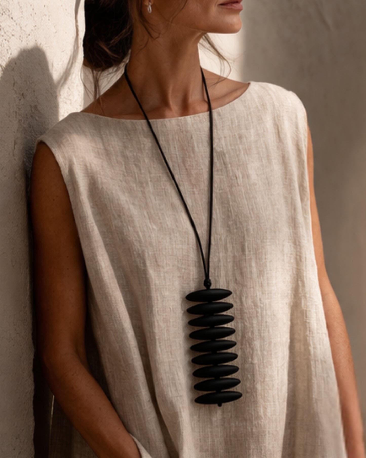 Model wearing the jen kahn Assegai Pendant with black resin beads on a leather cord over a natural linen garment.