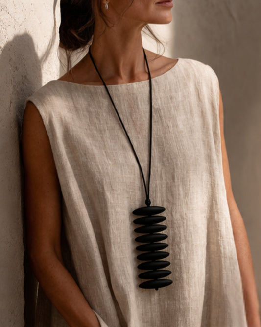 Model wearing the jen kahn Assegai Pendant with black resin beads on a leather cord over a natural linen garment.